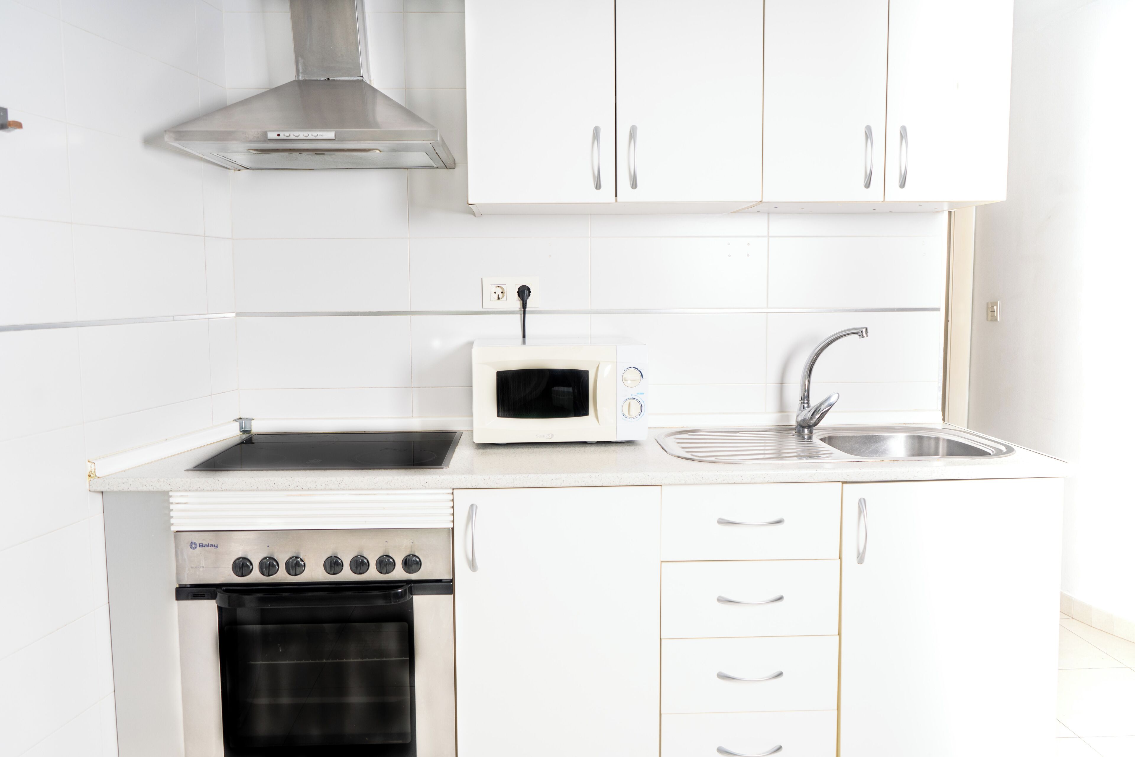 Una cocina compacta con horno integrado, microondas y pileta de acero inoxidable.