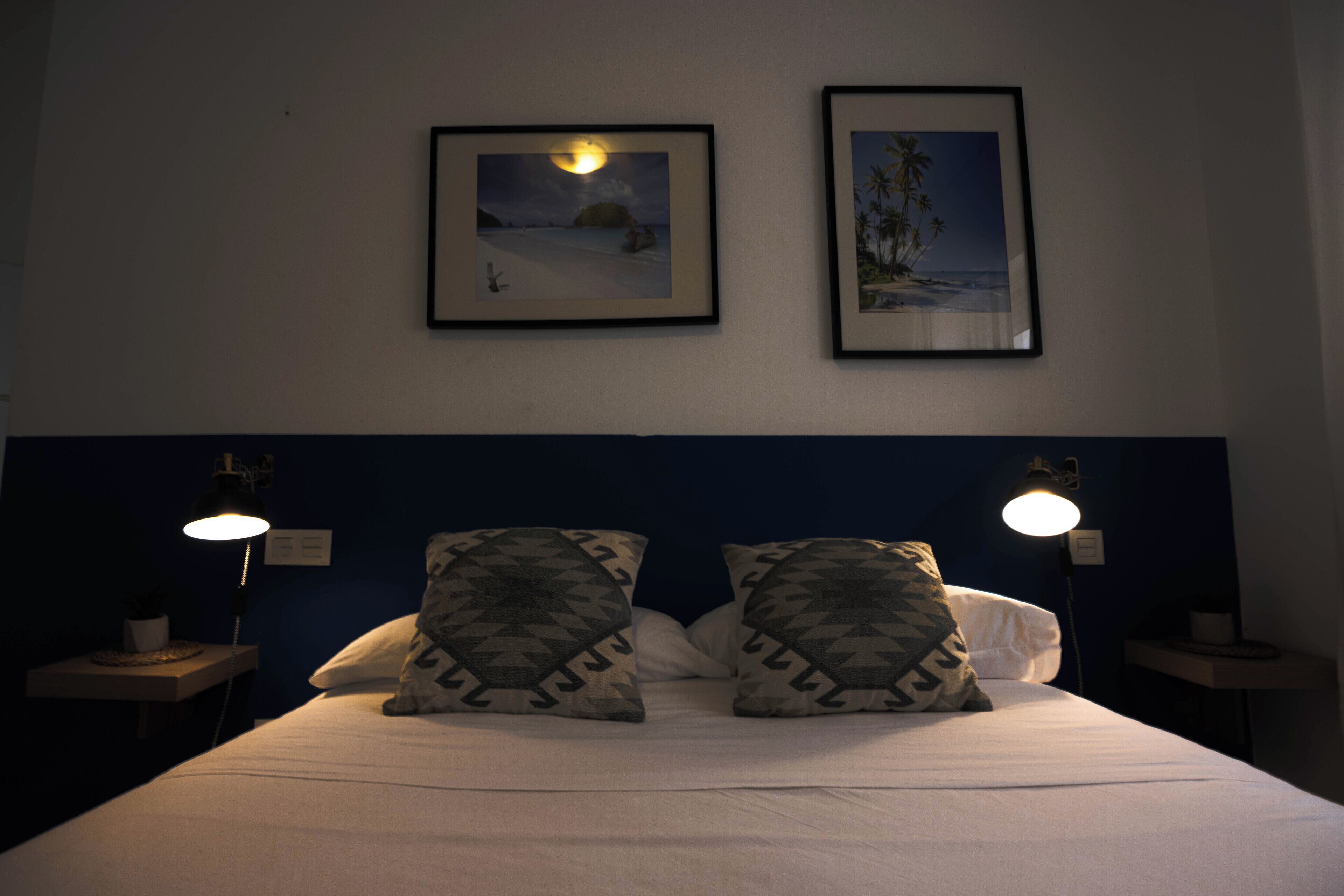 A hotel room with a bed, two nightstands, two wall-mounted lamps, and two framed pictures on the wall.
