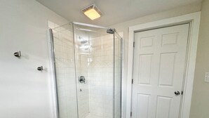 A corner bathroom with a glass-enclosed shower, white tiled walls, and a white door. - Trojan Hideaway on First Street (Upland)