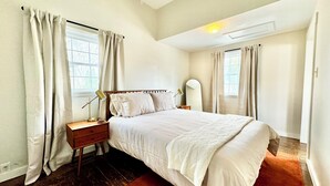 A bedroom with a bed, nightstand, lamp, and a mirror. - Trojan Hideaway on First Street (Upland)