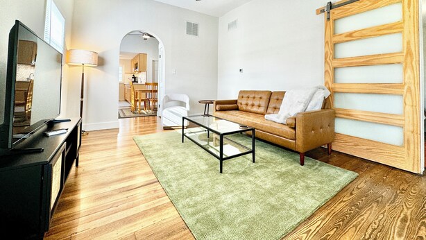 A living room with a sofa, coffee table, TV, and a ceiling fan. - Trojan Hideaway on First Street (Upland)