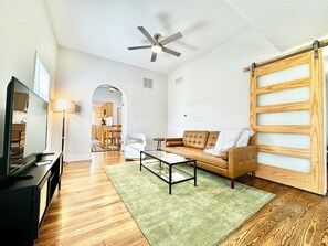 A living room with a sofa, coffee table, TV, and a ceiling fan. - Trojan Hideaway on First Street (Upland)