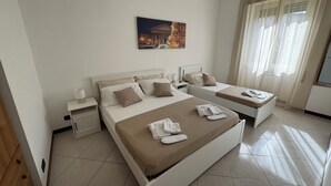 A hotel room with two beds, a nightstand, a lamp, a painting on the wall, and a window with curtains. - Elegant Apartment in the center of Rome (Roma)