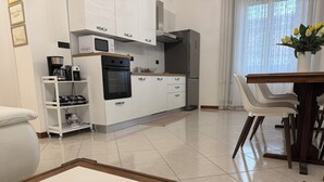 A modern kitchen with white cabinets, a black oven, and a coffee machine. There is a dining table with chairs and a vase of flowers. - Elegant Apartment in the center of Rome (Roma)