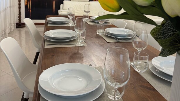 A dining area with a large cityscape mural, a chandelier, and white dining chairs. - Elegant Apartment in the center of Rome (Roma)