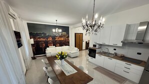 A modern kitchen with white cabinets, a wooden dining table, and a chandelier. - Elegant Apartment in the center of Rome (Roma)