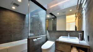 A modern bathroom with a glass-enclosed shower, a white bathtub, and a vanity with a sink and towel storage.
