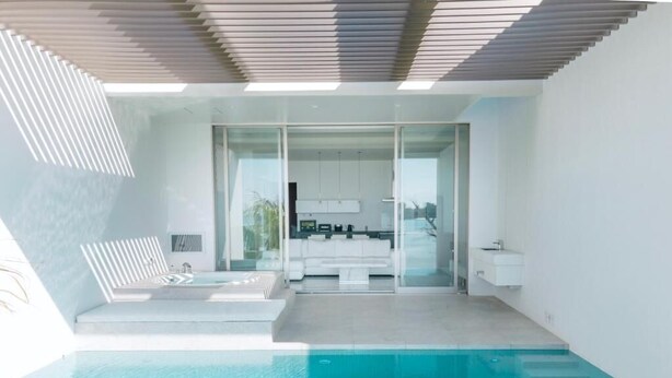 A modern indoor swimming pool with a glass wall leading to a kitchen area.