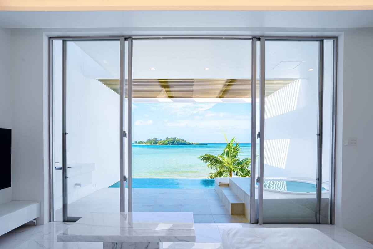 Habitación moderna con un amplio ventanal corredera que da a un balcón con piscina y vista al océano.