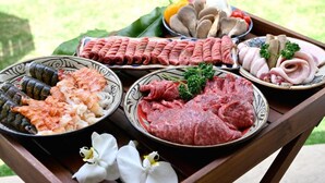 A tray with various types of raw meat and seafood, including shrimp, scallops, and different cuts of beef, displayed outdoors.