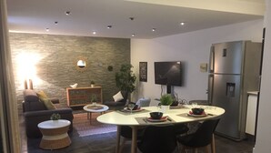 Una sala de estar moderna con una pared de piedra, un sofá, una mesa de centro y una zona de comedor con una mesa preparada para cuatro personas.