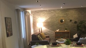 Una sala de estar moderna con comedor, que presenta una pared de piedra, un sofá, una mesa de centro y una mesa de comedor preparada para cuatro.