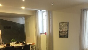 Una sala de estar moderna con comedor, una mesita redonda de mimbre, un sillón estampado y una alfombra colorida.
