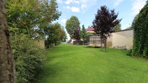 A well-maintained grassy yard with a trampoline, trees, and a building with a red roof in the background. - Mr. Grey by the lake (Zeuthen)