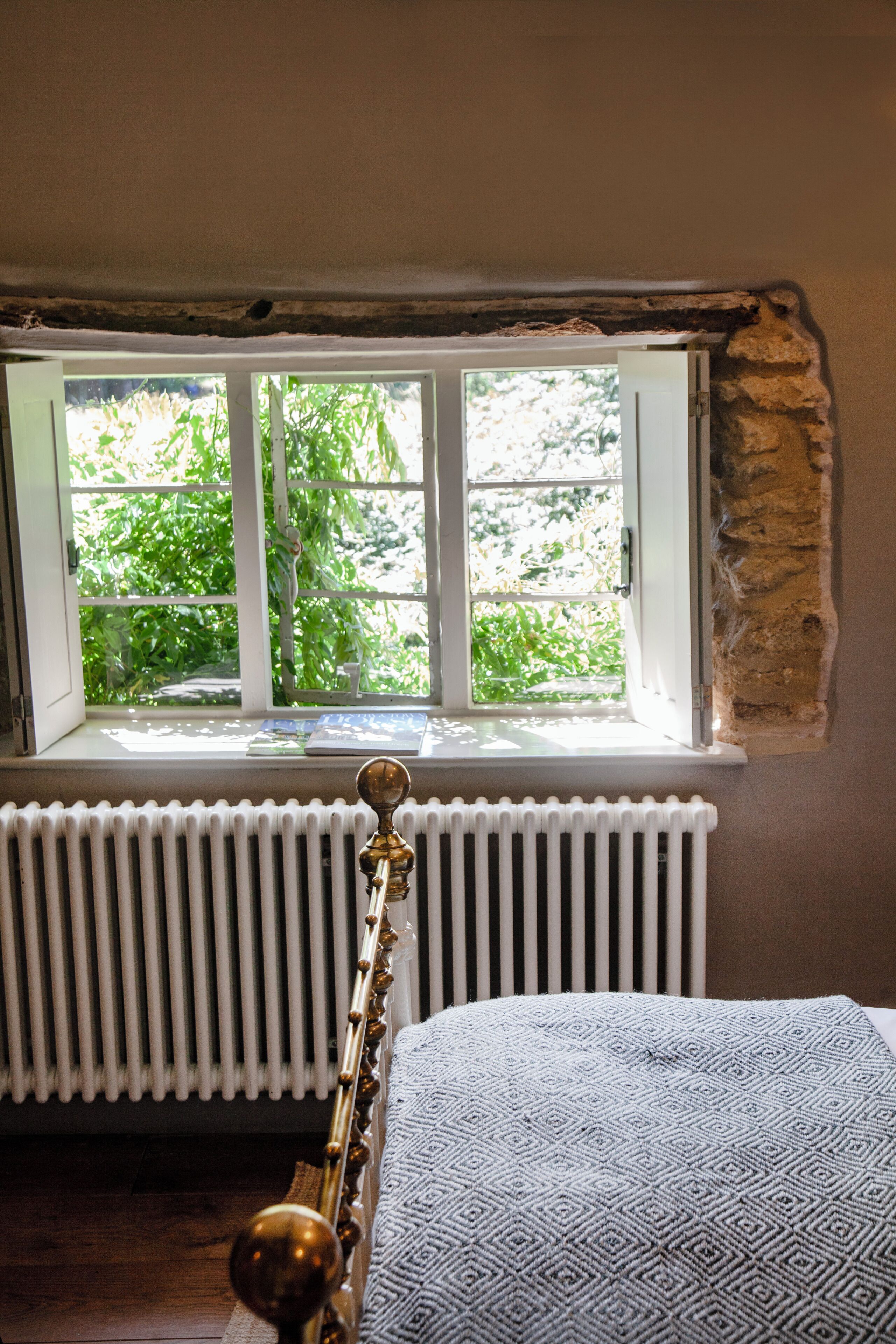 Quarto com radiador, janela com vista para o verde e cama com manta estampada.