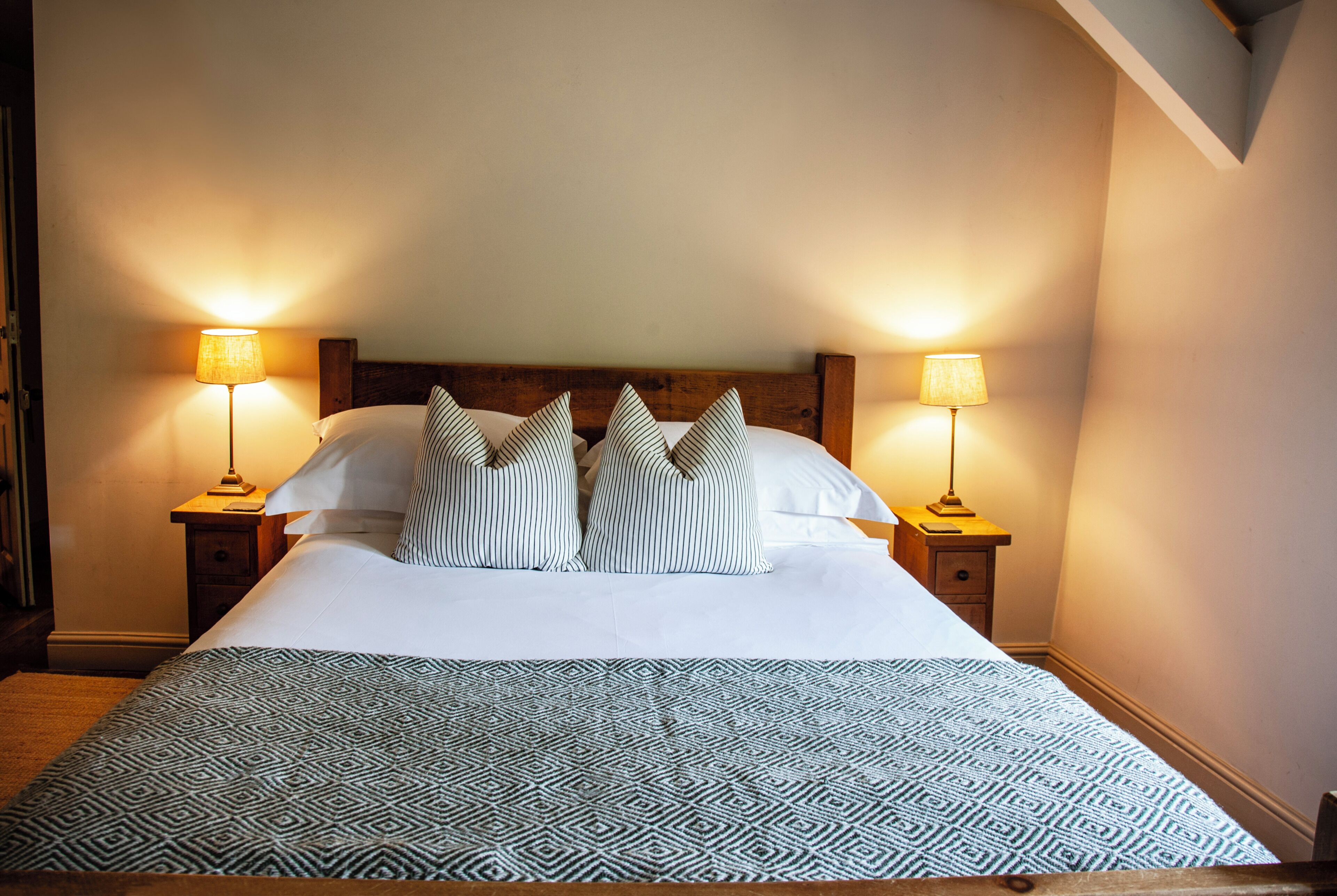 Un lit bien fait, avec des oreillers à rayures, deux lampes de chevet et une couvre-lit à motifs.