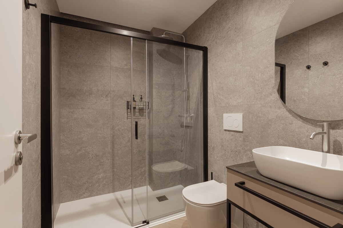 Ein modernes Badezimmer mit einer Duschkabine, einem weißen Waschbecken und einer Toilette.