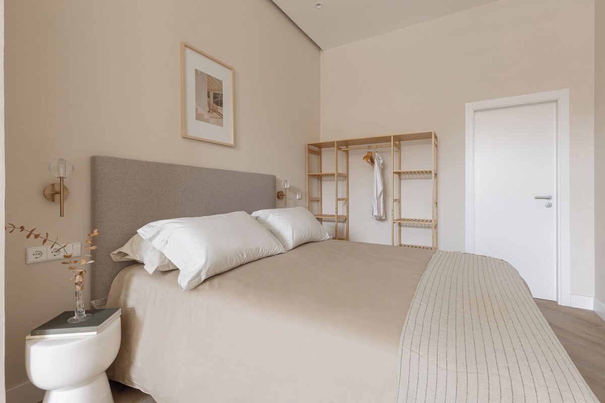 A bedroom with a large bed, a bedside table with a vase, a wardrobe, and a door.