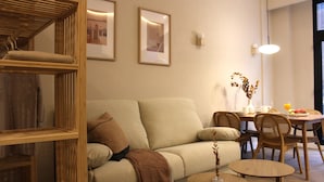 En stue med en sofa, et spisebord med stole og et reol i træ.