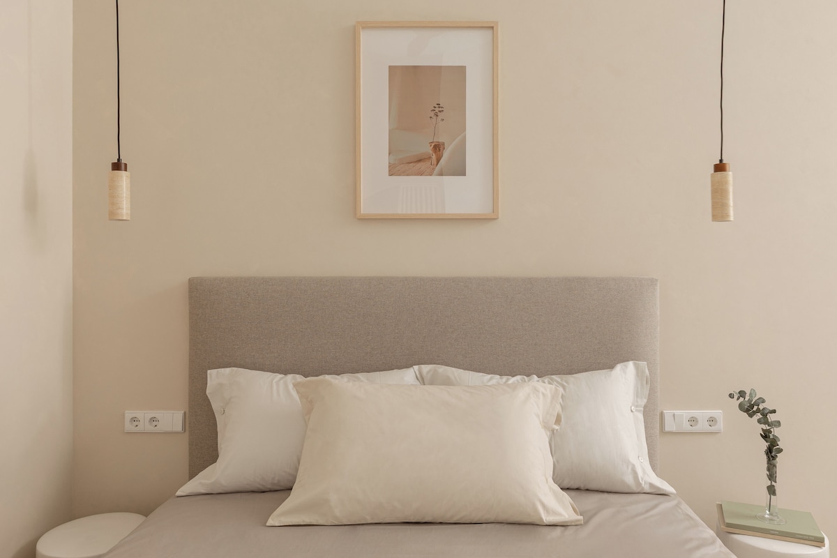 A neatly arranged bedroom with a bed, pillows, bedside table, and a framed picture on the wall.