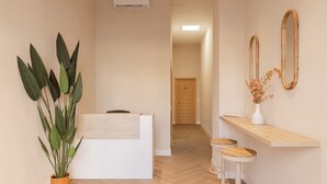 Et receptionområde med en receptionsdisk, en potteplante, to træbøtter og et spejl på væggen.