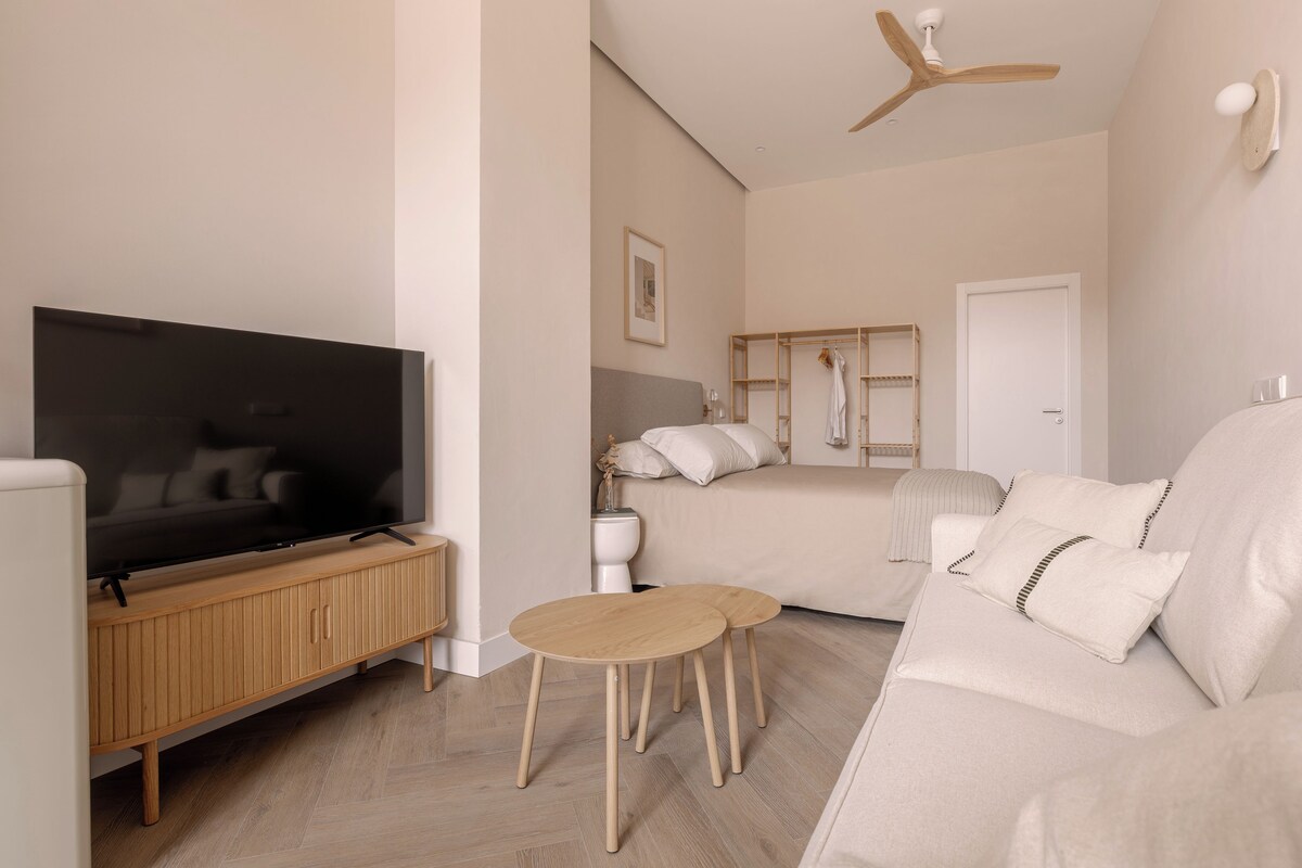 A modern living room with a flat-screen TV, wooden furniture, a sofa, and a ceiling fan.