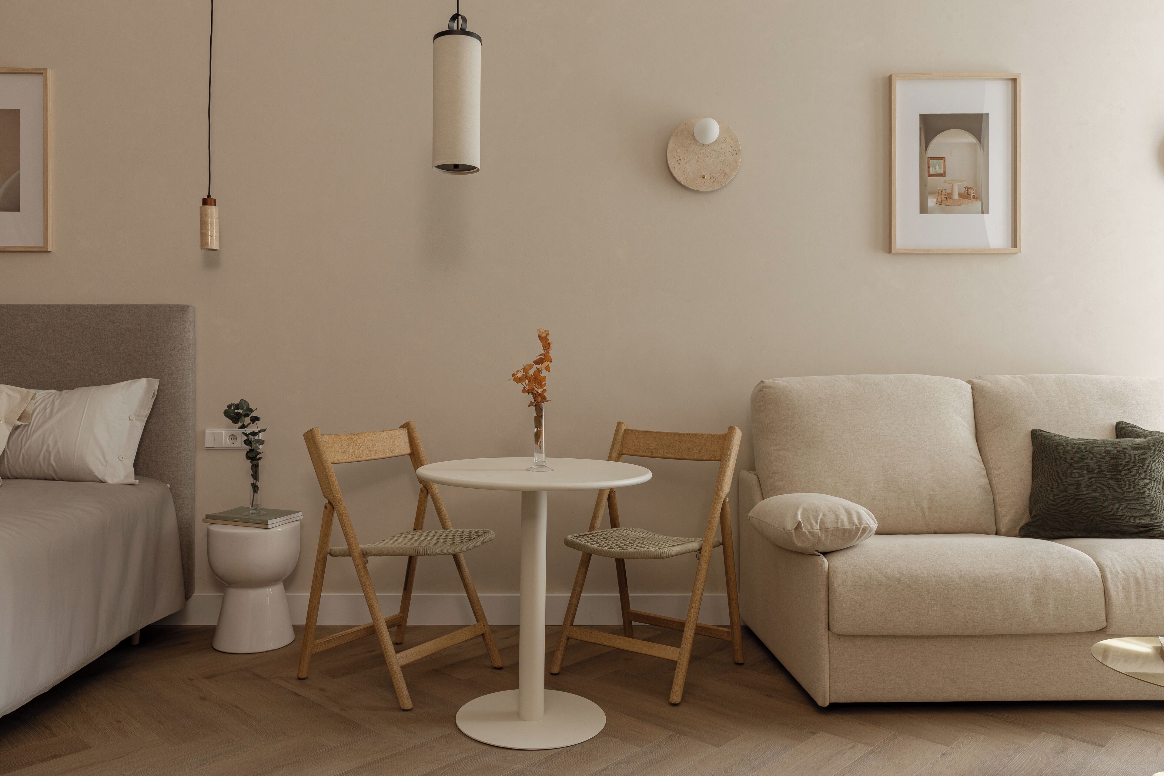 A minimalist living room with a round table, two chairs, a sofa, a bedside table, and a small decorative plant.