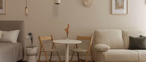 A minimalist living room with a round table, two chairs, a sofa, a bedside table, and a small decorative plant.