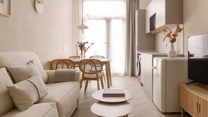 En moderne stue med sofa, spisebord med stole, et køkken med et køleskab og et fjernsyn.