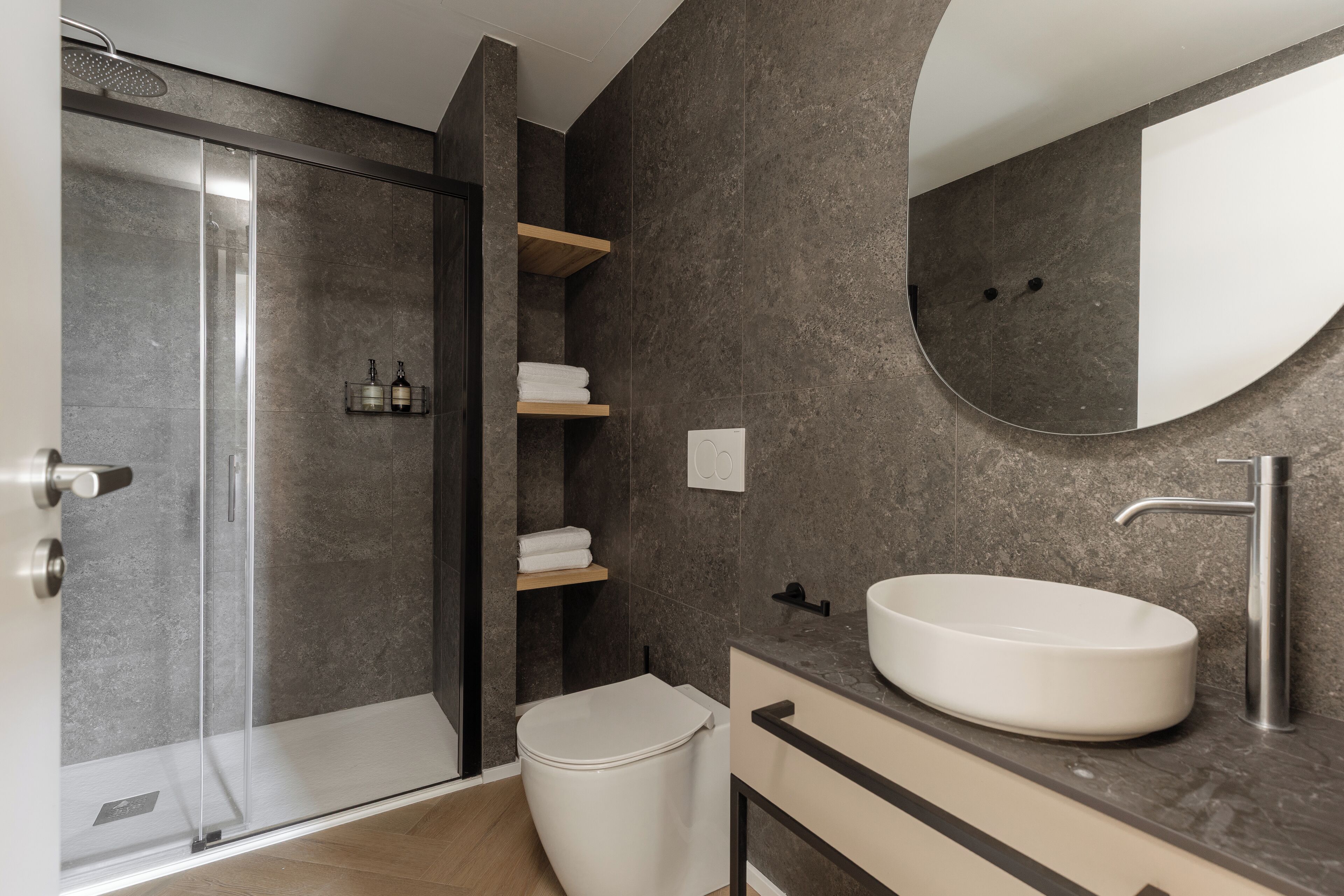 A modern bathroom with a glass-enclosed shower, a white toilet, a large oval sink, and a mirror.