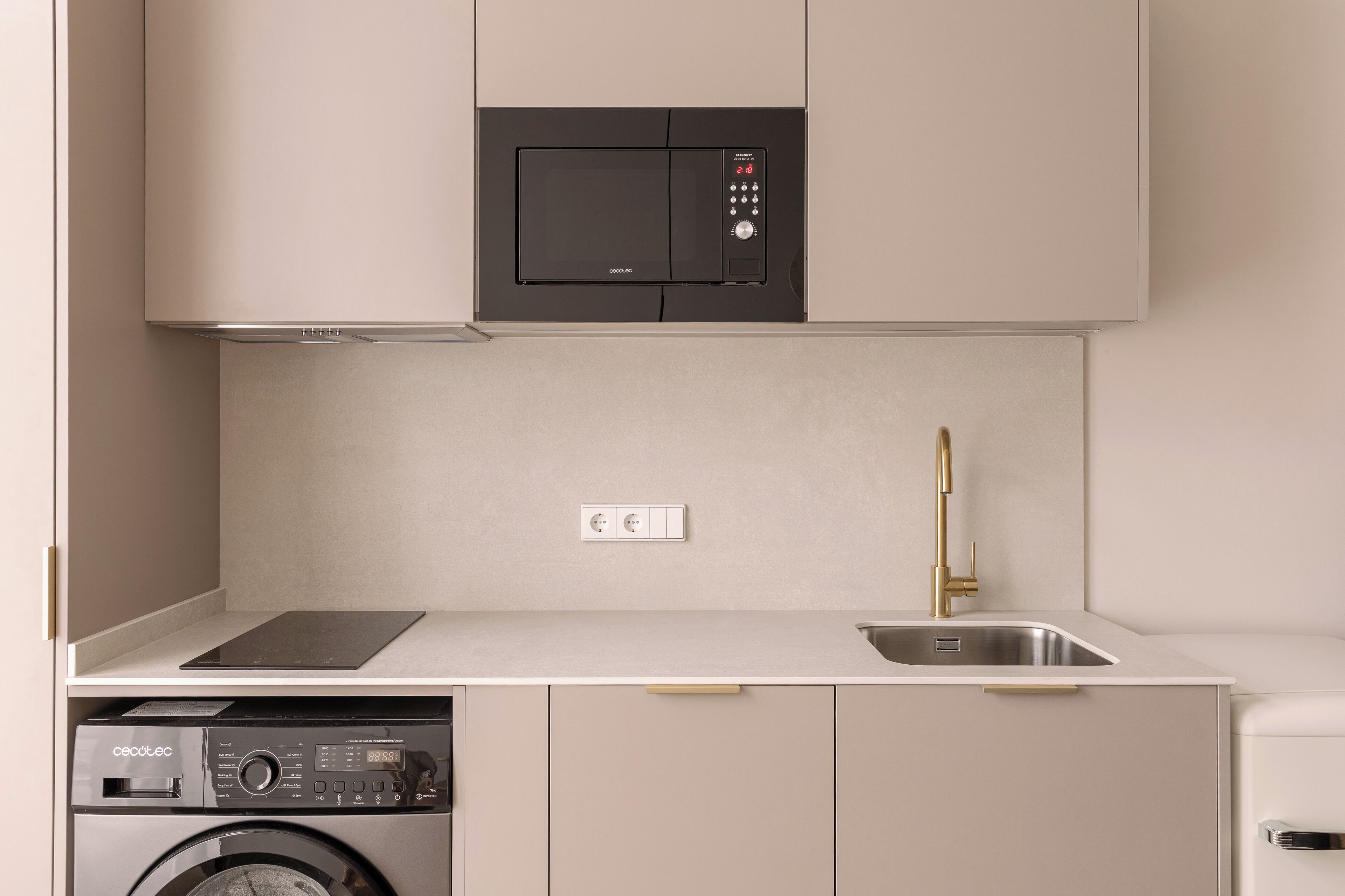 A compact kitchen with a built-in microwave, a washing machine, and a sink with a gold faucet.