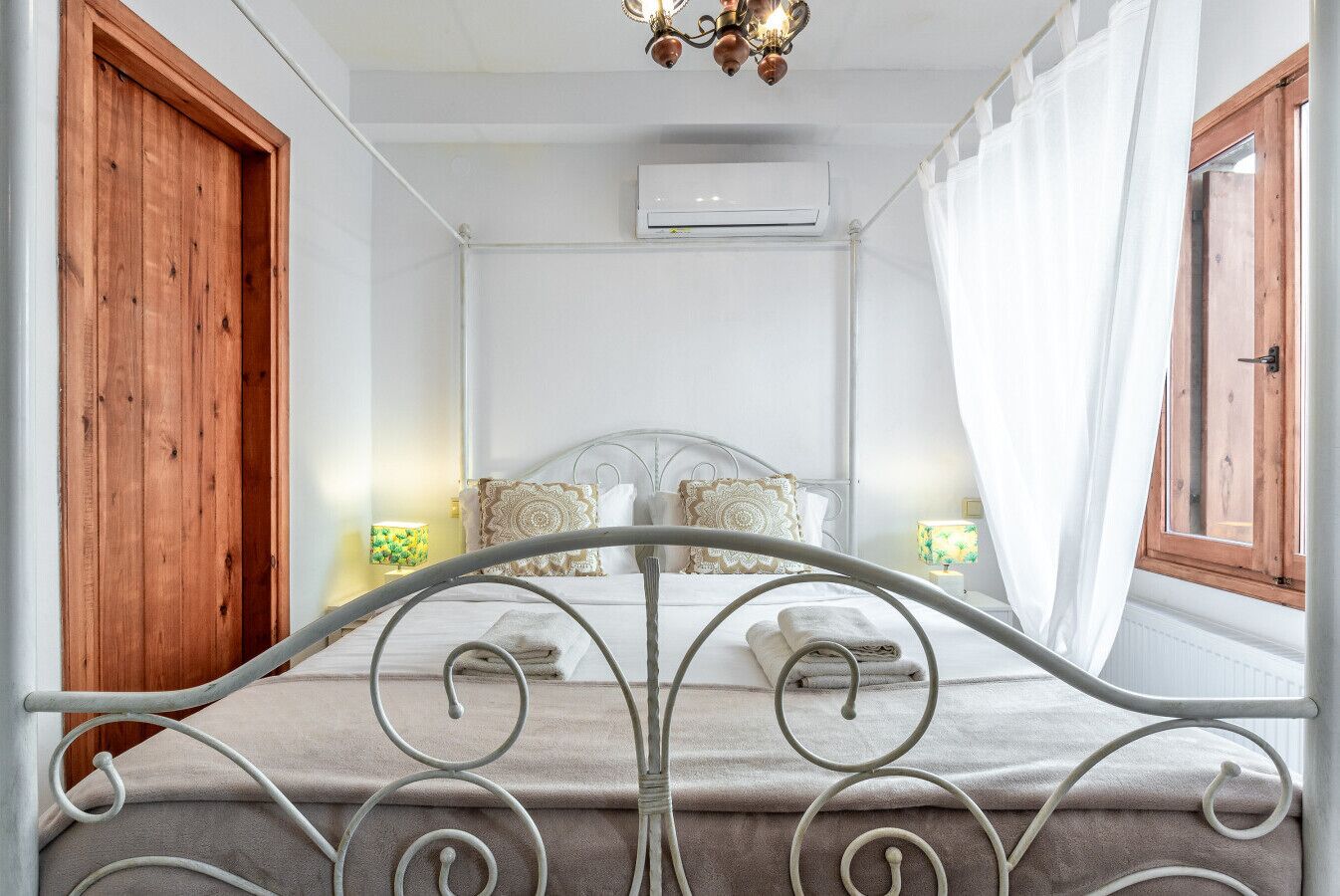 Ein Schlafzimmer mit Metallbett, weißen Wänden, einer Holztür und einer Klimaanlage.