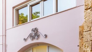 Un edificio rosa con una entrada arqueada blanca, una pared de piedra a la derecha y un pequeño escalón que lleva a la puerta.