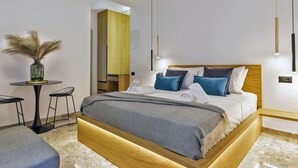 Una habitación de hotel moderna con una cama de madera, una pequeña mesa redonda con sillas, un jarrón con plantas secas y un armario de madera.