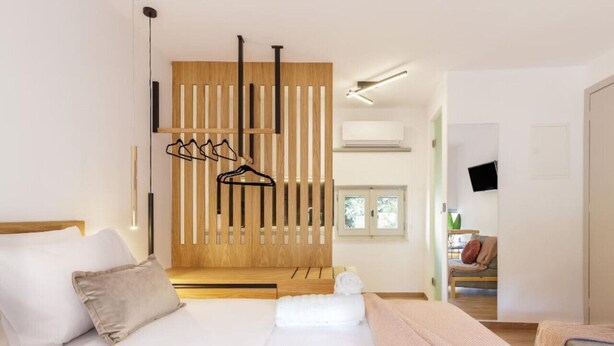 A modern hotel room with a large bed, a wooden partition, and a view of the outside.