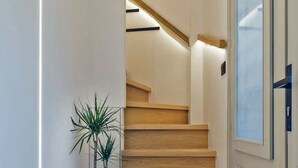 A staircase with wooden steps leading to a landing, a potted plant on the landing, and a door with a frosted glass panel. - Arch.4 Luxury Living (Chania)