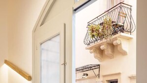 A staircase leading to a door with a frosted glass panel, a balcony with a wrought iron railing and flowers, and a cobblestone street outside. - Arch.4 Luxury Living (Chania)