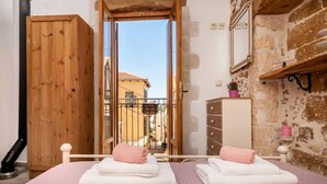 Ein Schlafzimmer mit Bett, einem Holzschrank, einem Schminktisch und einem Balkon mit Blick auf Gebäude.
