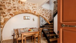 Ein Essbereich mit Steinwand, Holztisch und Stühlen. Eine Treppe mit schwarzer Geländer ist sichtbar.