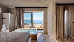 A modern bedroom with a large bed, a bathtub, and a view of the sea. - Nami Suites | Alenia (Ravdoucha)