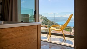 A room with a wooden cabinet and a yellow chair by a large window overlooking a scenic view. - Nami Suites | Alenia (Ravdoucha)