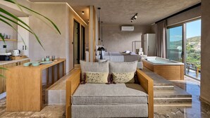 A modern living room with a sofa, a coffee table, and a view of a balcony. - Nami Suites | Alenia (Ravdoucha)