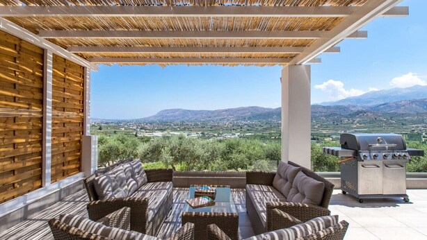 An outdoor patio with wicker furniture, a grill, and a view of the countryside. - Casa Galatas | Private pool |The Wisers Living (Chania)