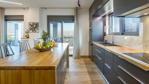 A modern kitchen with a wooden island, dark cabinetry, and a view of the city. - Casa Galatas | Private pool |The Wisers Living (Chania)