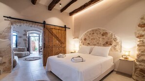 A bedroom with a large bed, a wooden barn door, a stone wall, and a rustic ceiling. - Delta-Rho | Kalami | Crete (Kalami)