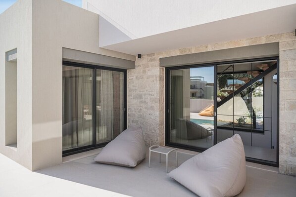 A modern outdoor seating area with a pool, stone walls, and large sliding glass doors.