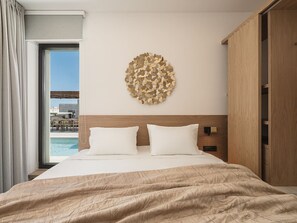 A hotel room with a large bed, a wooden headboard, a circular wall decoration, and a view of a pool and buildings outside.