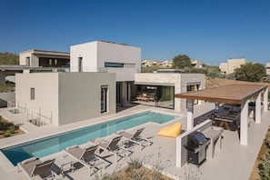 A modern house with a swimming pool, outdoor seating, and a barbecue area.