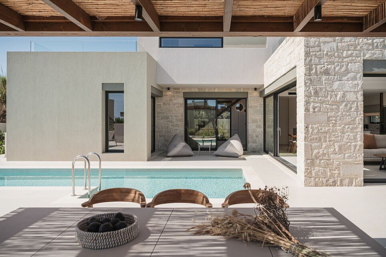 A modern outdoor pool area with a minimalist design, including a pool, lounge chairs, and a stone wall.