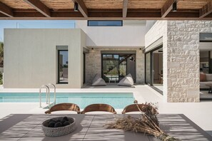 A modern outdoor pool area with a minimalist design, including a pool, lounge chairs, and a stone wall.